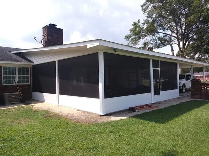 A screened-in patio addition with white framing and black mesh screens attached to a brick house with a chimney.
