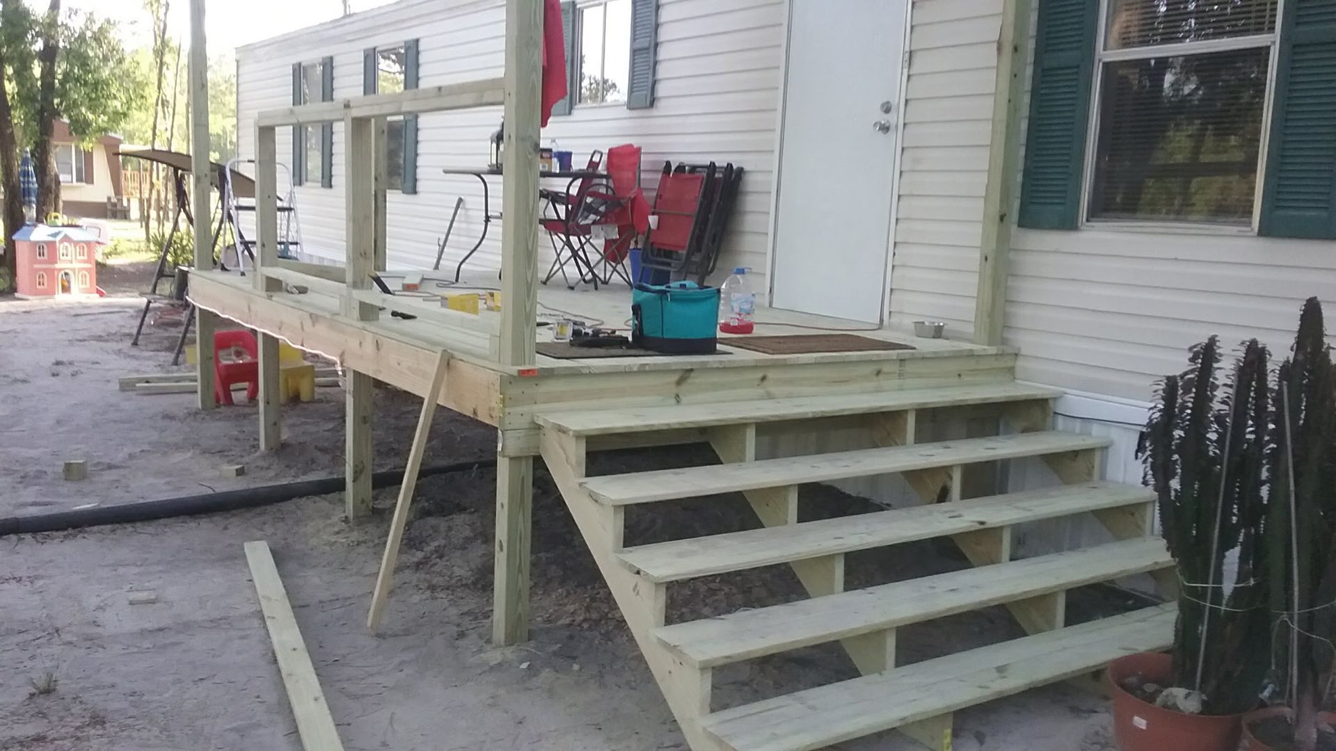 A light-colored wooden porch and staircase under construction attached to the side of a light-colored mobile home.
