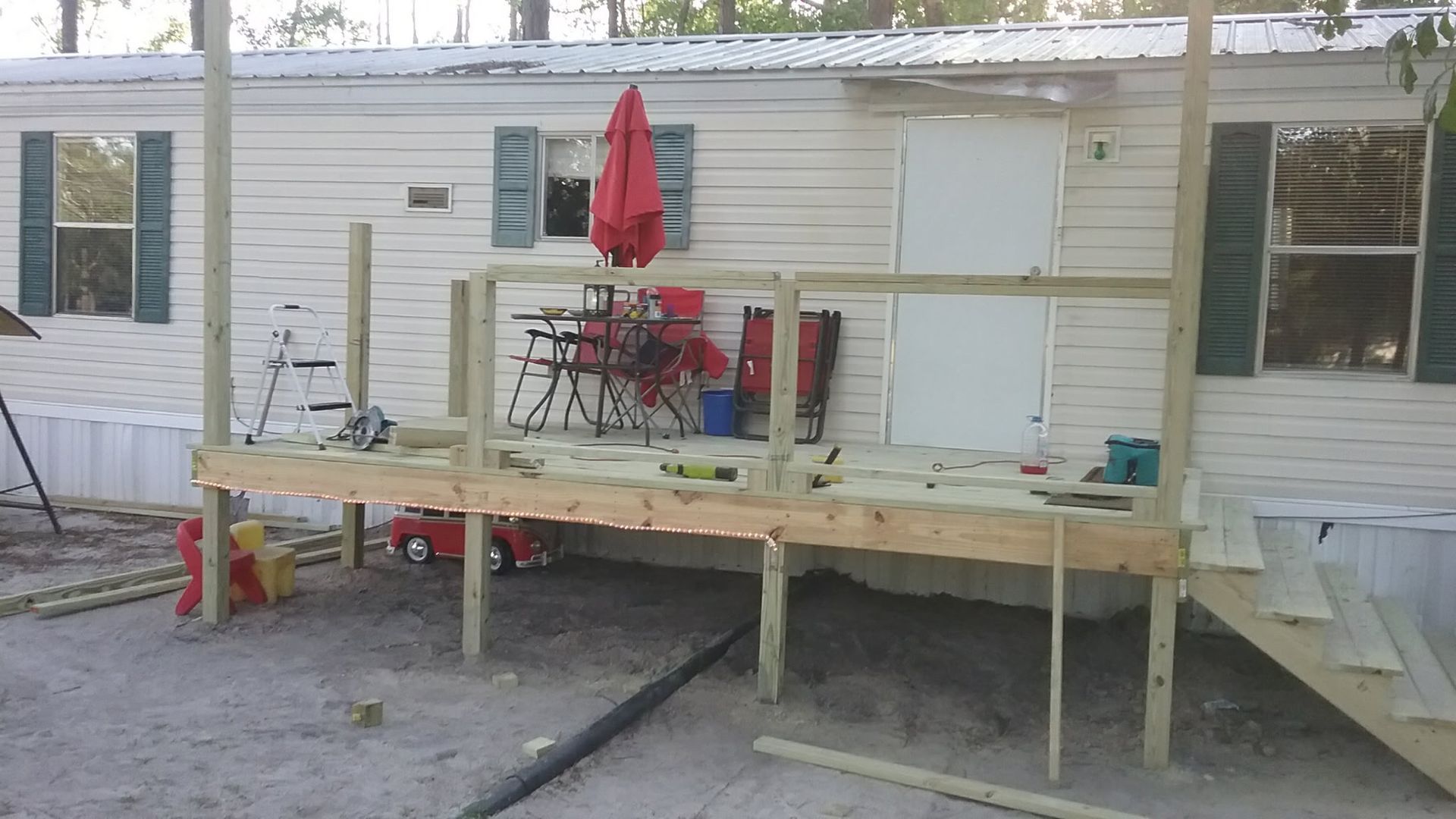 A new, unfinished wooden deck being built in front of a white mobile home with green shutters.