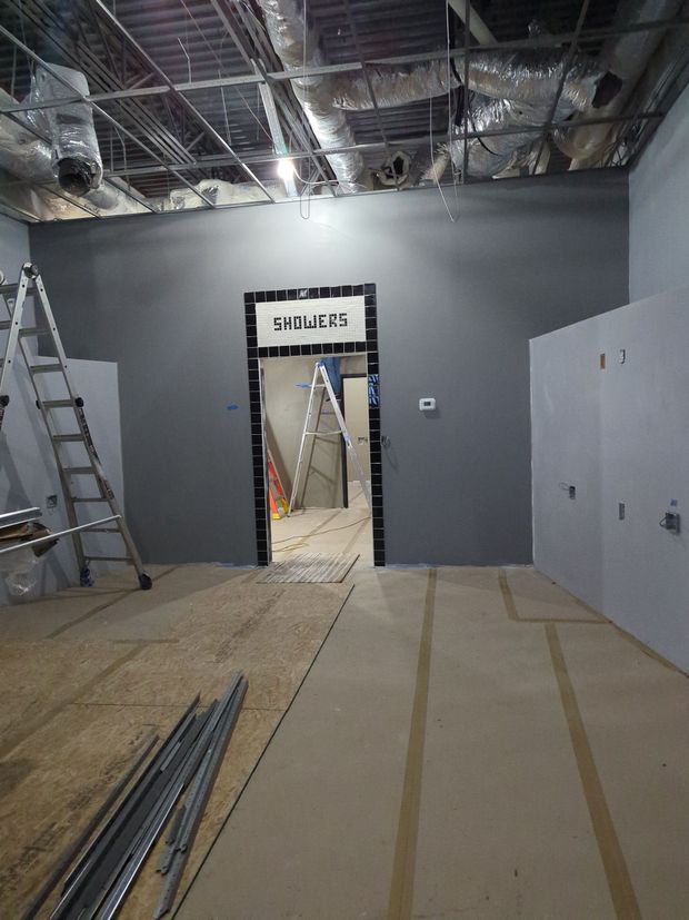 A room under construction with grey walls, an open doorway, a ladder on the left, and exposed ceiling ductwork.