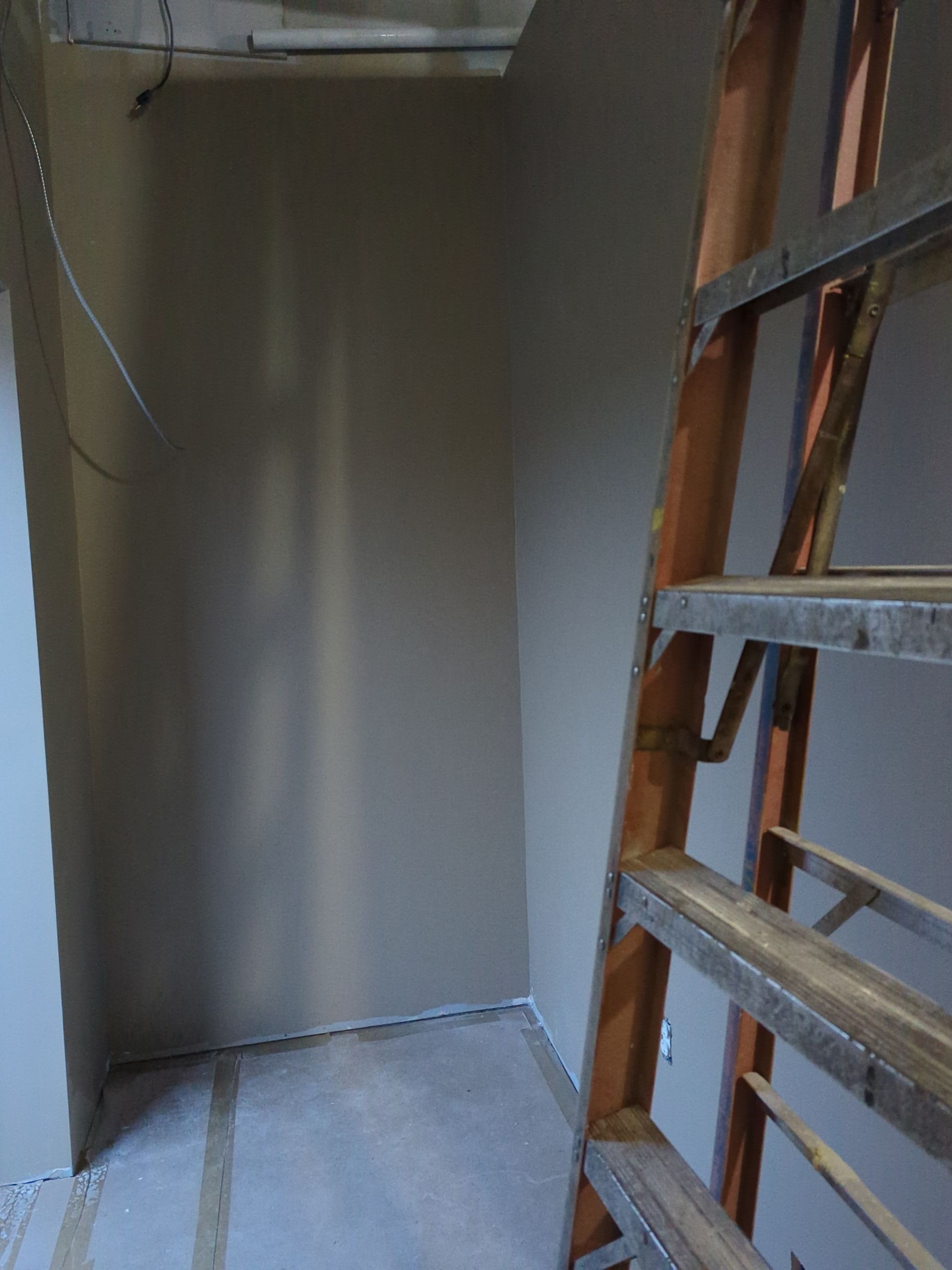 An interior view of a room under construction with gray-painted walls, a concrete floor, and a wooden stepladder.