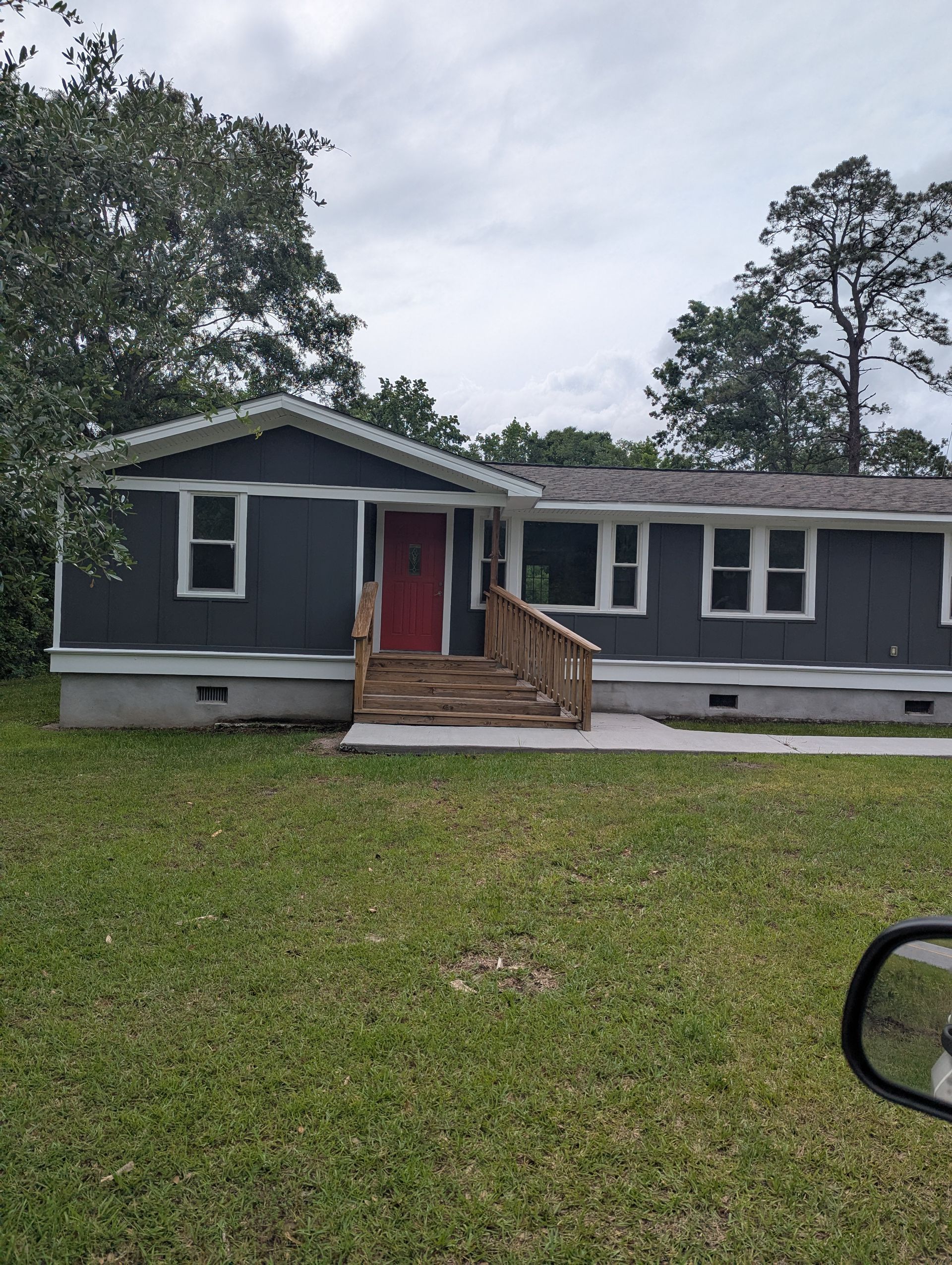 A single-story modular home with dark gray siding, a bright red front door, and a wooden porch in a grassy yard.