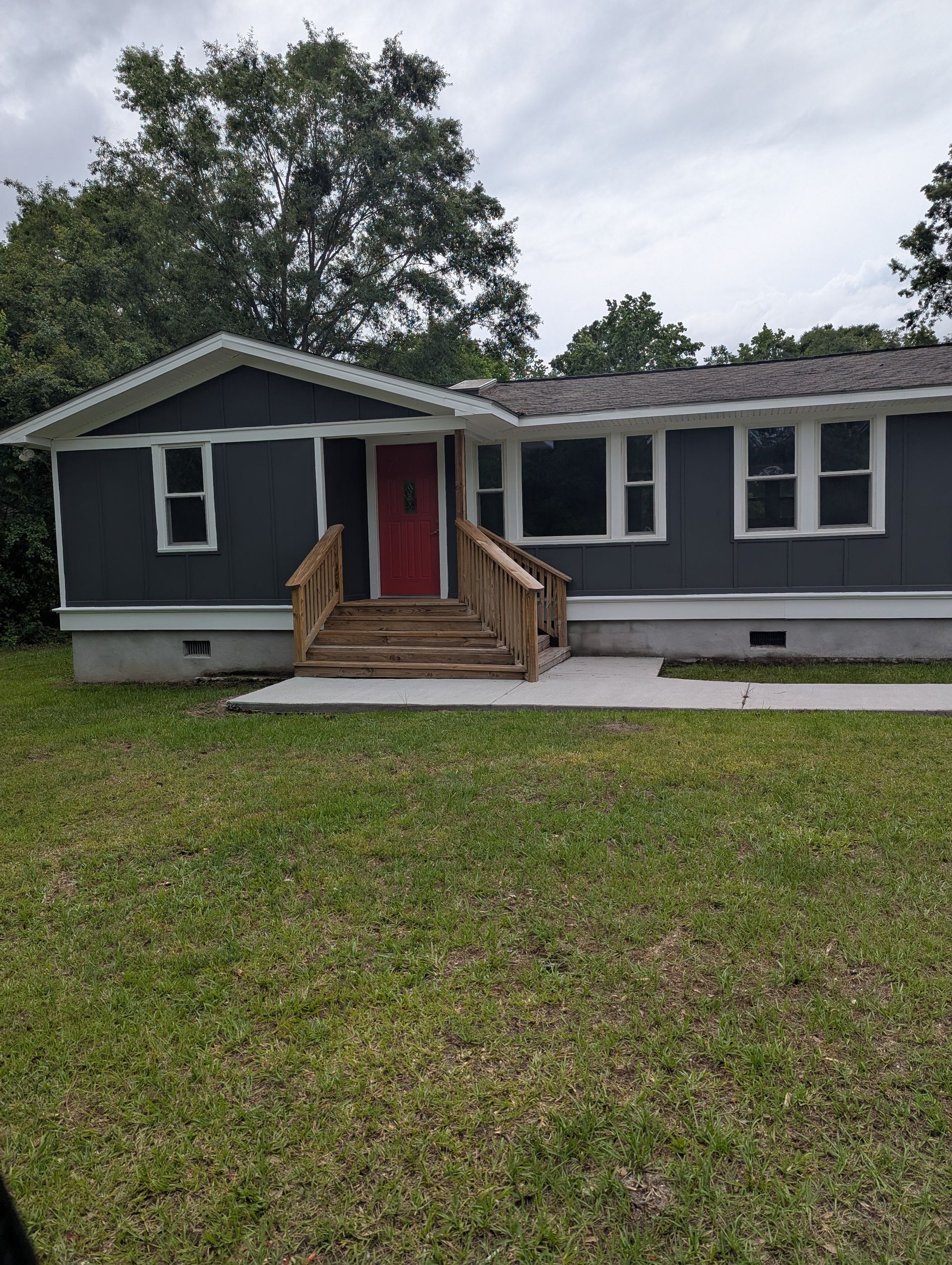 A dark gray single-story house with a red front door, white trim, and a wooden front staircase.