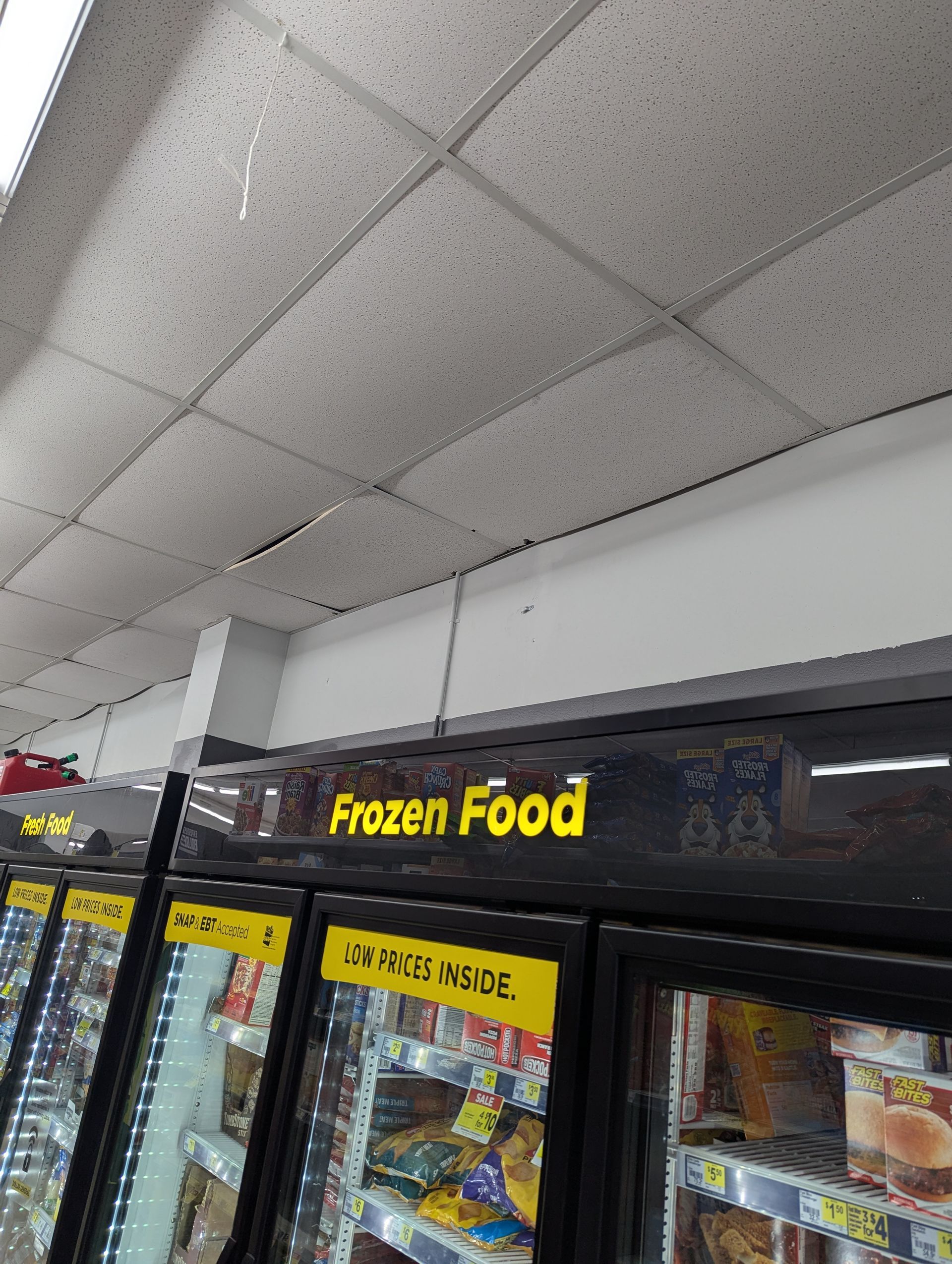 Low-angle view of a store’s frozen food aisle with bright yellow signage and white ceiling tiles.