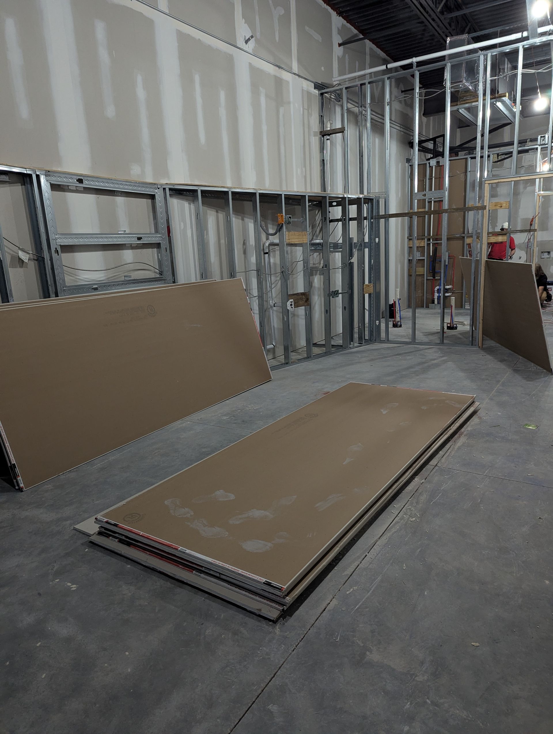 Construction site interior with metal wall framing, unpainted drywall sheets on the floor, and unfinished walls.