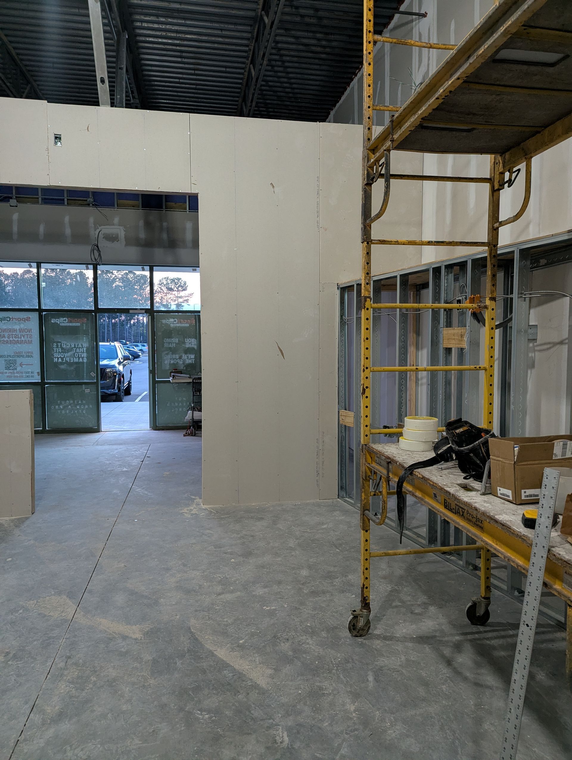 Interior construction site with a yellow metal scaffold, unfinished drywall partitions, and a glass entrance door.
