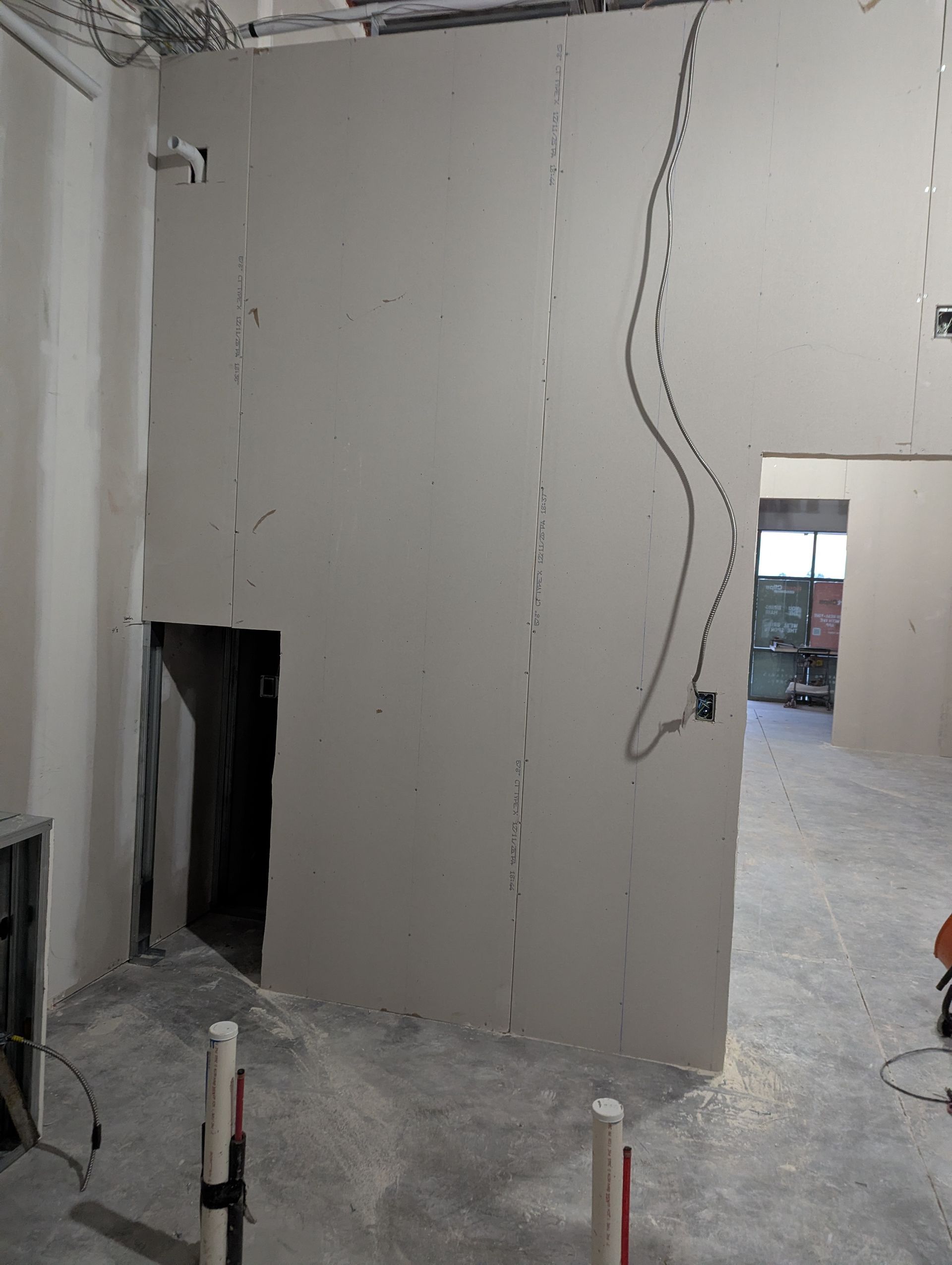 An interior construction site showing a drywall partition wall with electrical wiring and an unfinished opening.