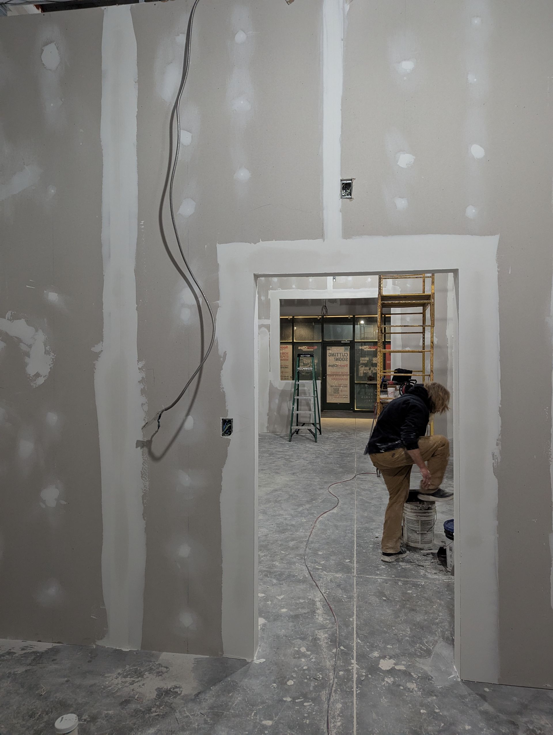 A person works in a doorway of a room under construction with unfinished drywall and visible electrical wiring.