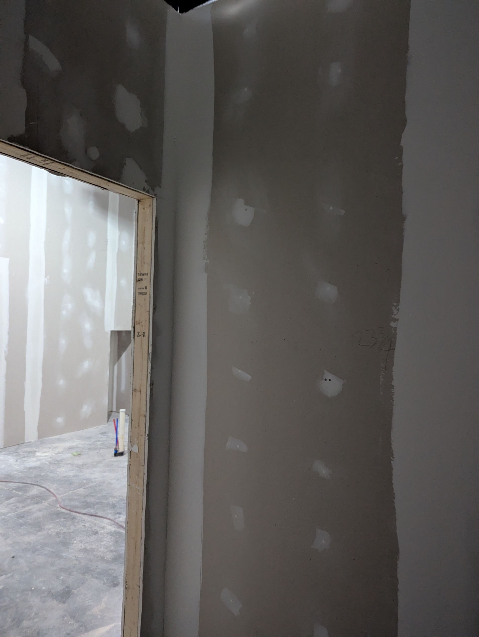 An interior view of a room under construction with unfinished drywall, exposed wooden studs, and taped joints.