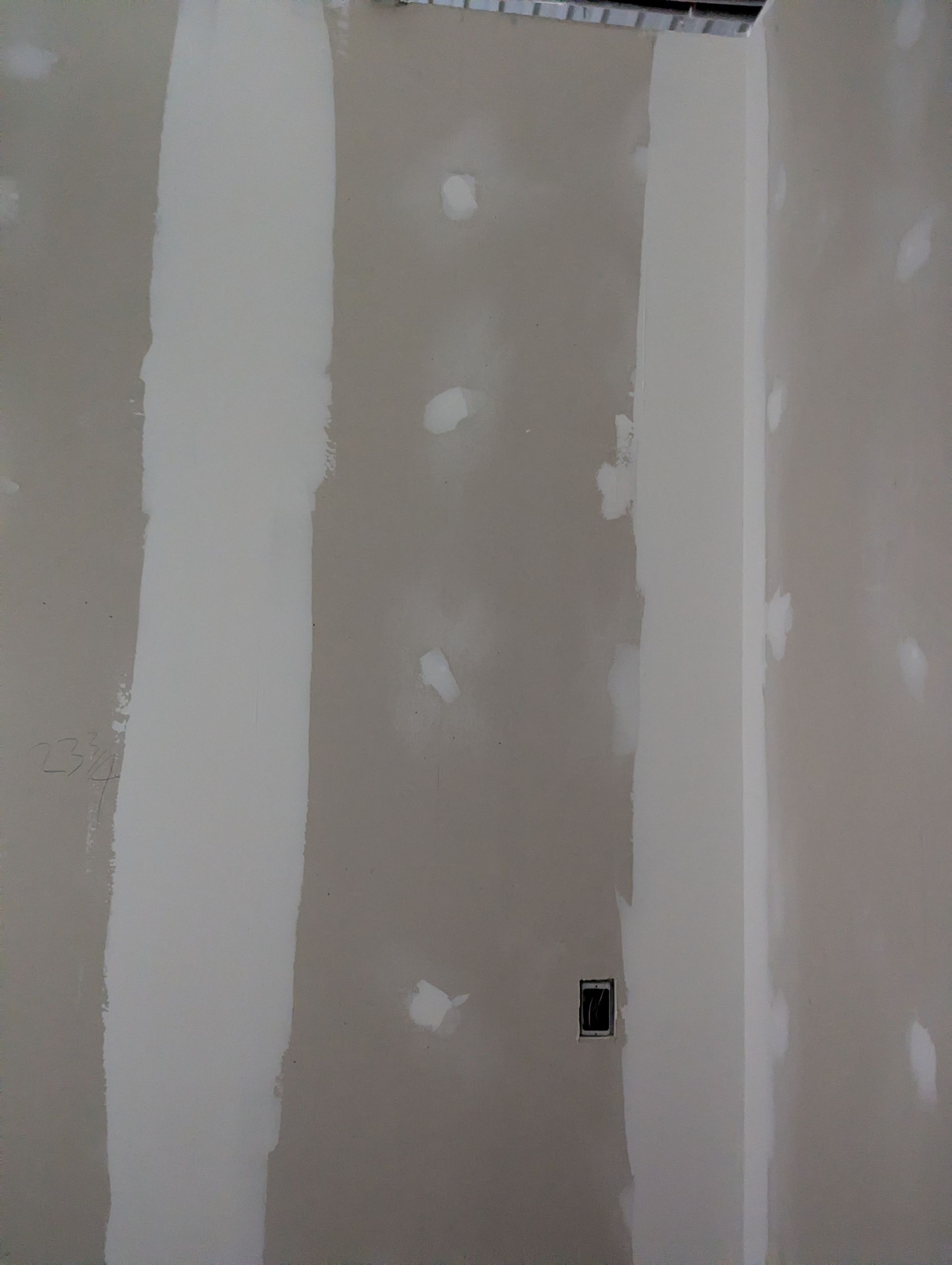 A wall with unfinished drywall, showing taped seams and filled screw holes.