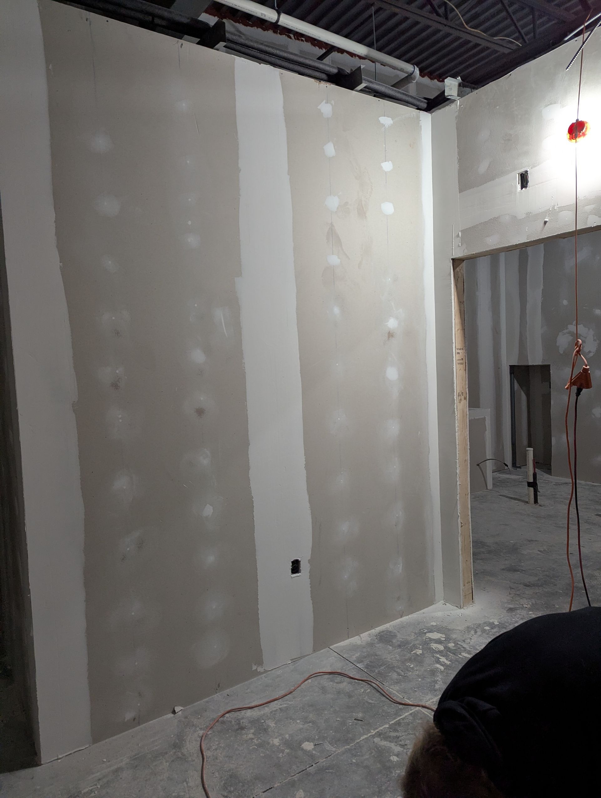 Construction site showing a newly installed drywall wall with taped seams, joints, and visible screw indentations.
