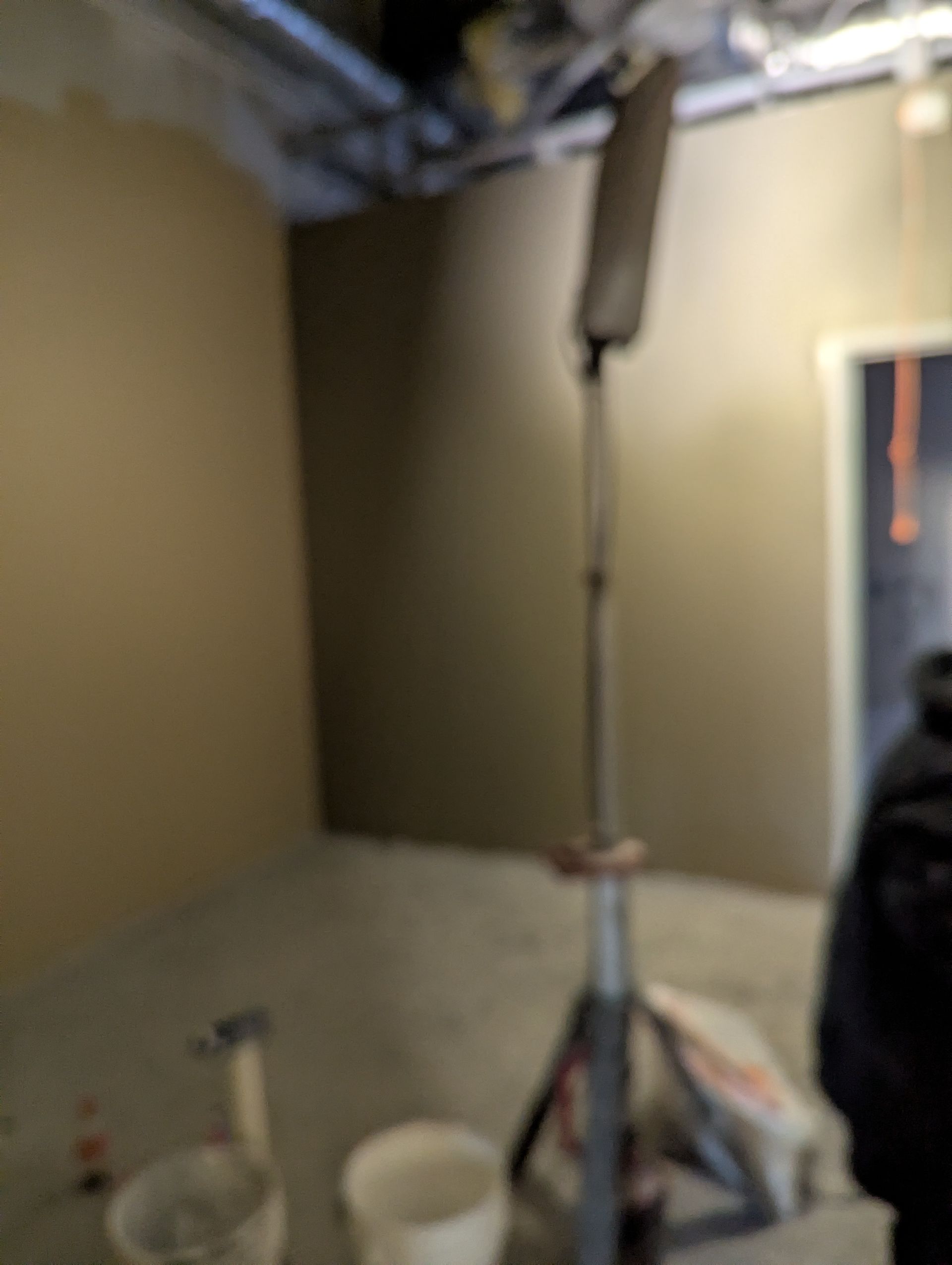 A tall industrial tripod stand holds a light fixture in a room under construction, with buckets on the concrete floor.