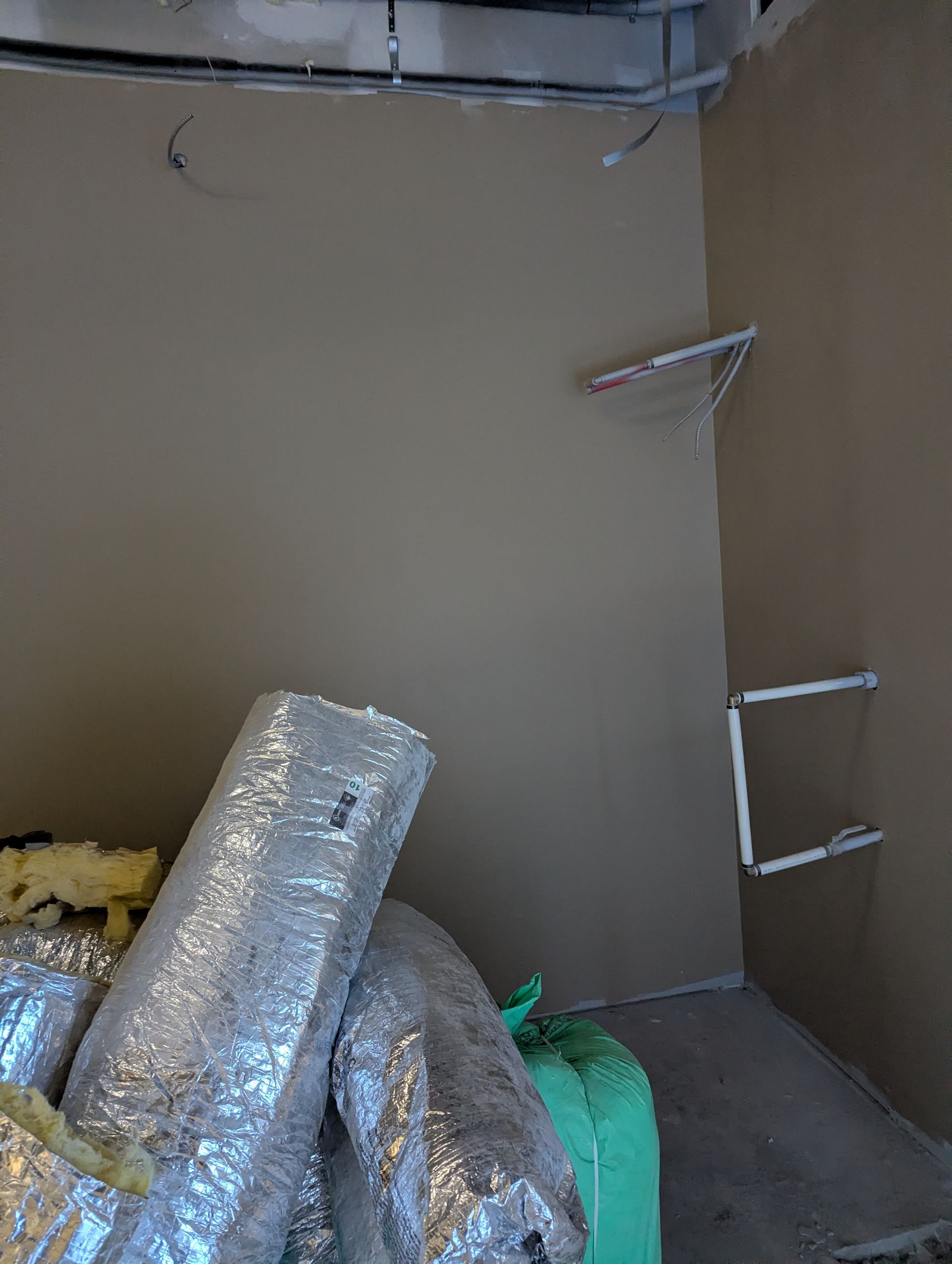 An unfinished room with beige walls, exposed ceiling wiring, and large rolls of foil-wrapped insulation in the foreground.