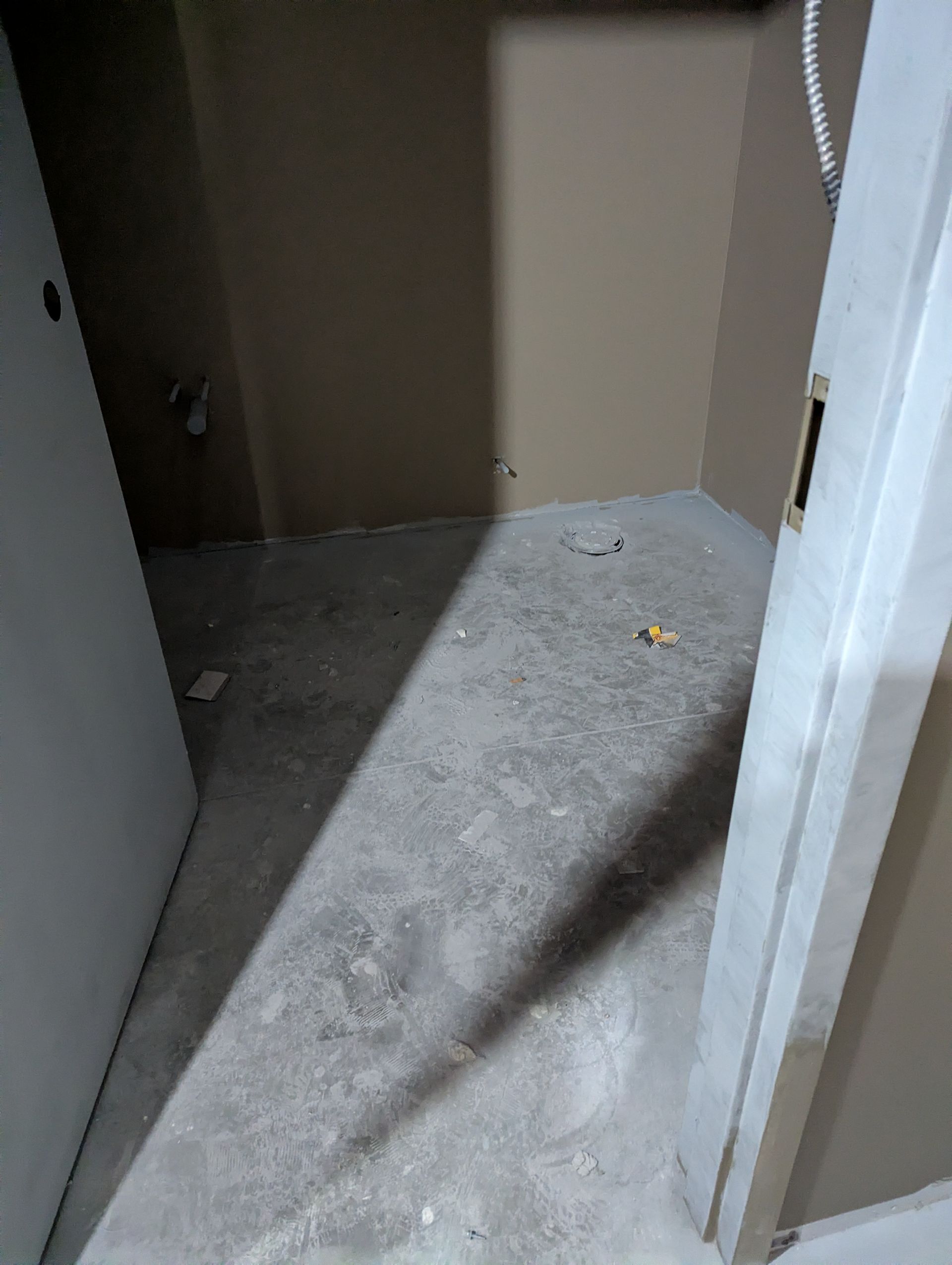 An unfinished walk-in closet with beige walls, a concrete floor, and an open doorway.