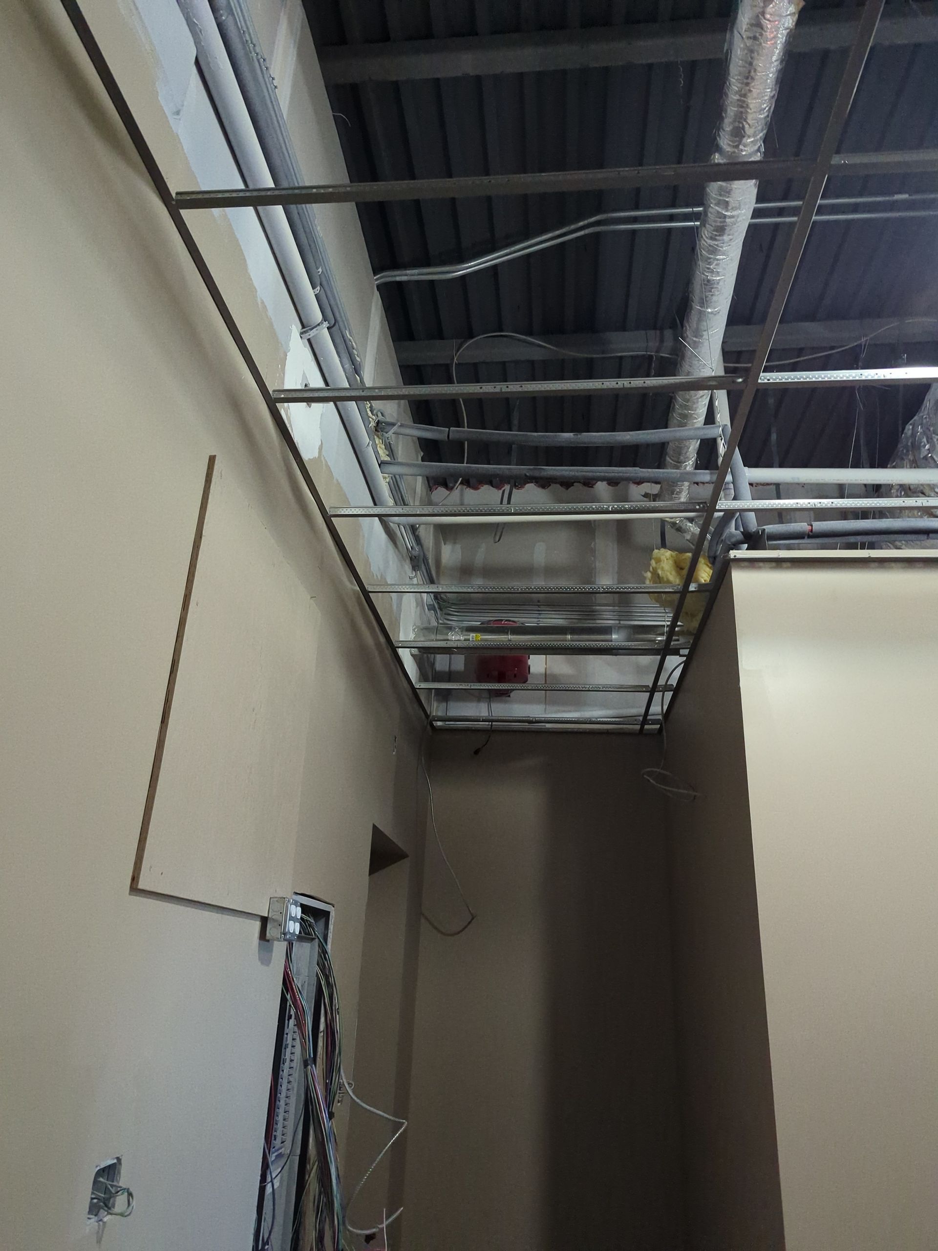 A view of a narrow interior corridor under construction, showing exposed ceiling metal framing and utilities.