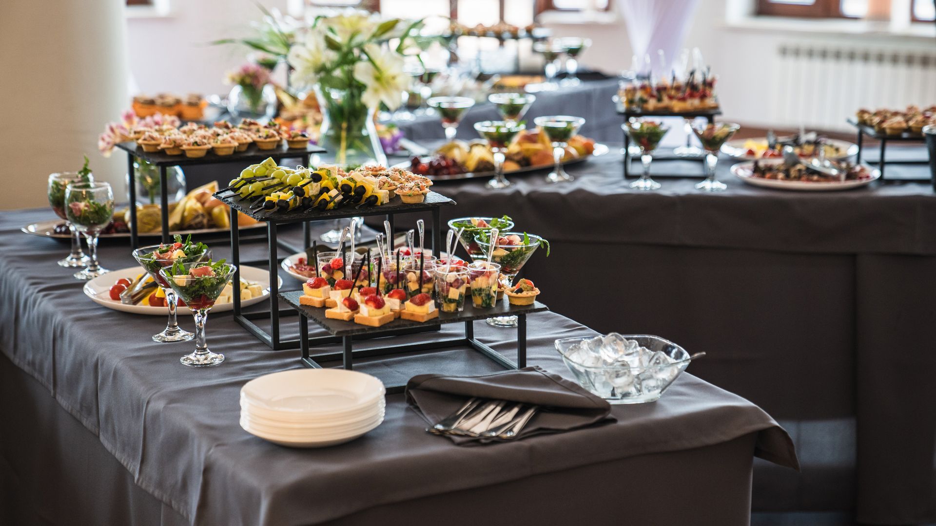 Buffet table with assorted appetizers, desserts, and plates on black tablecloths in a bright dining room