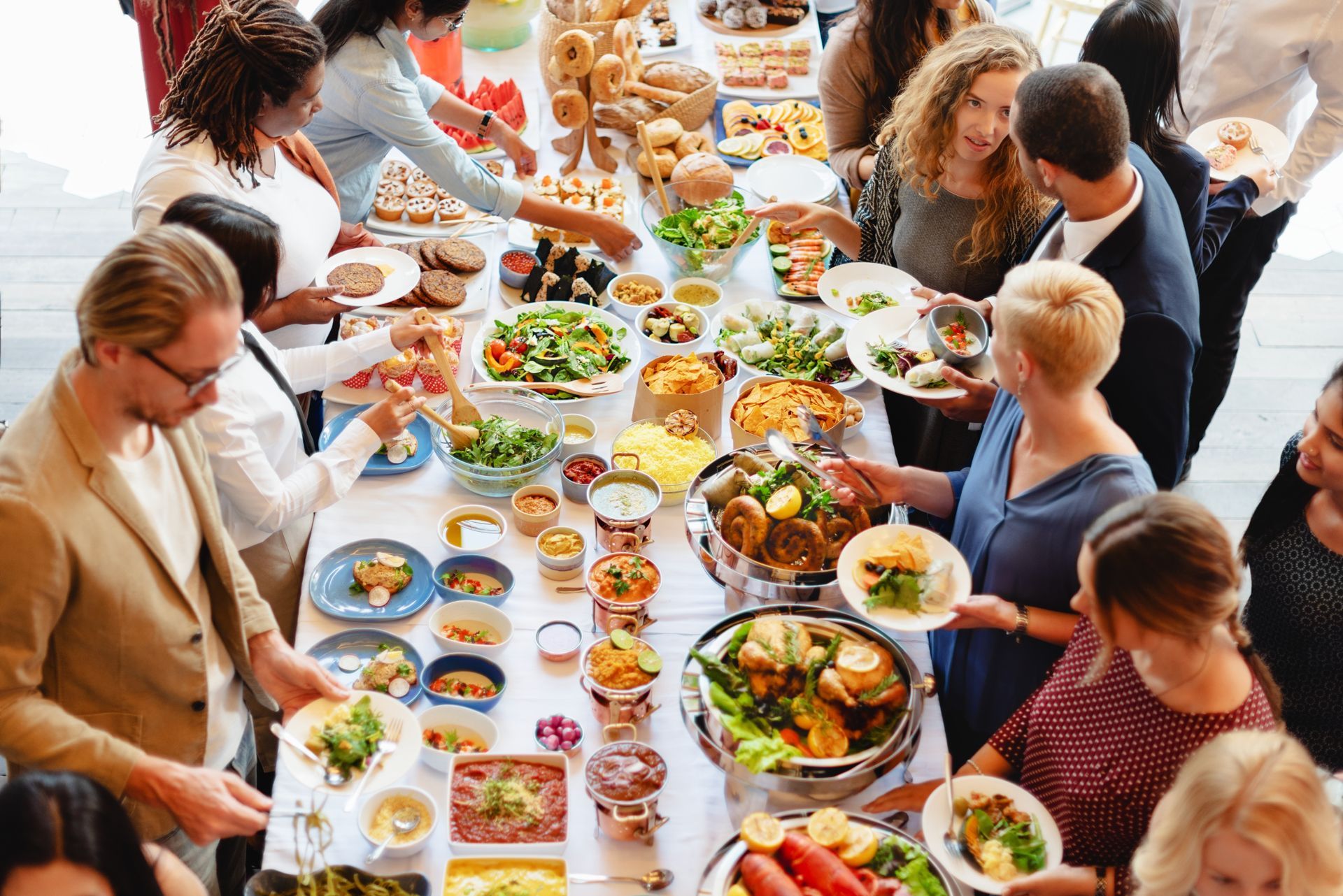 People gathered around a long table serving and eating colorful dishes at a lively shared meal