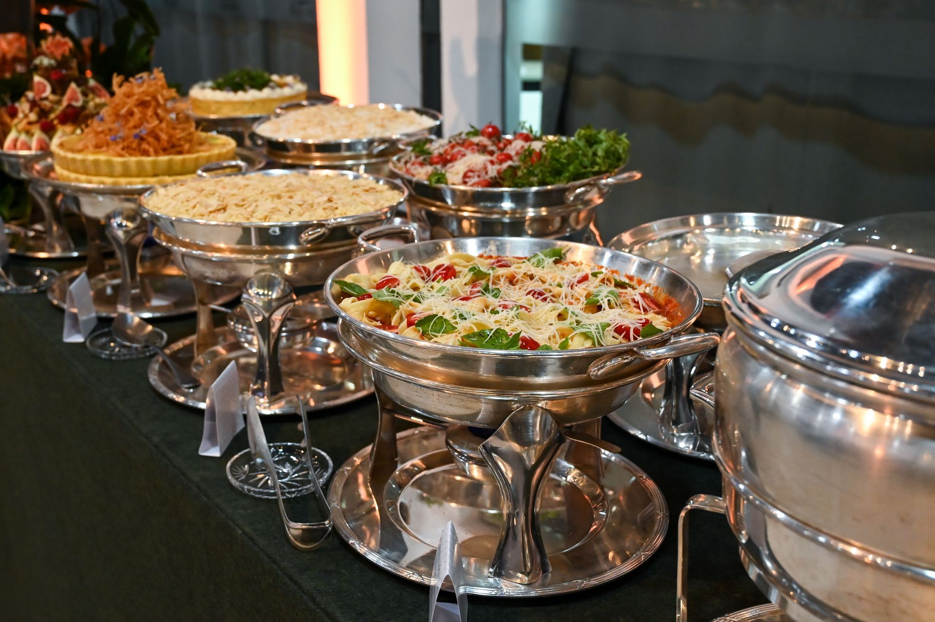 Buffet table with silver chafing dishes and bowls of salad and appetizers