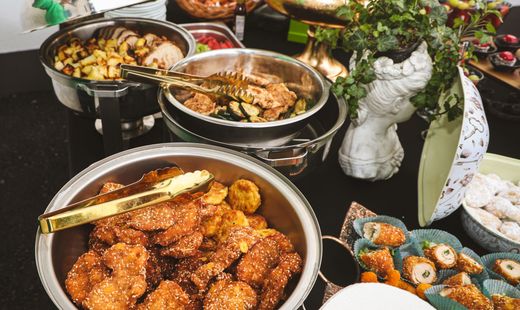 Buffet table with assorted food trays, sushi, roasted dishes, and floral centerpieces