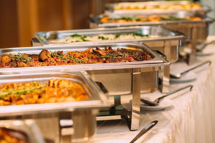 Buffet table with covered trays of assorted hot dishes in a bright dining setting