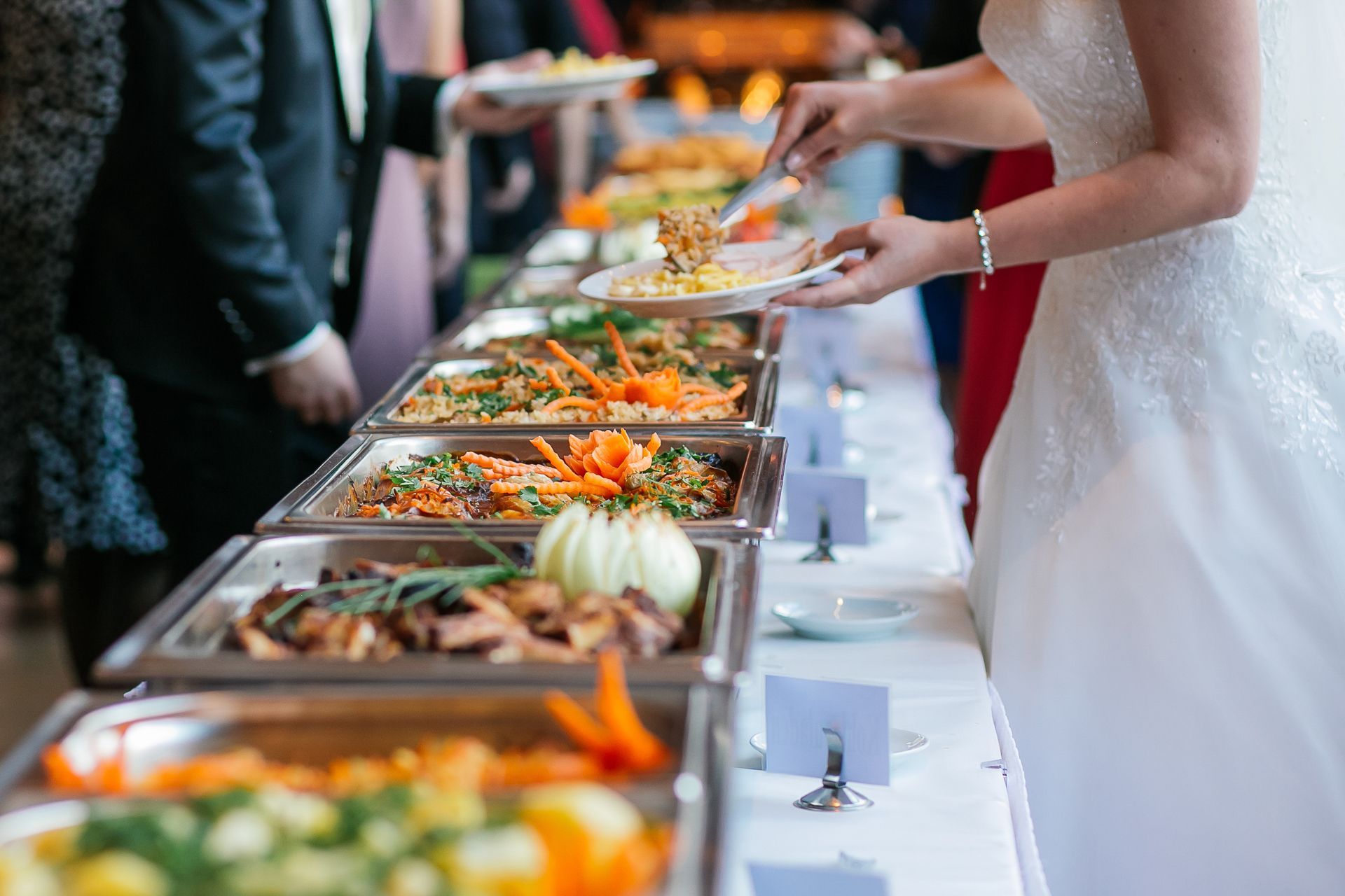Guests serving themselves from a buffet table with trays of colorful food at a formal event