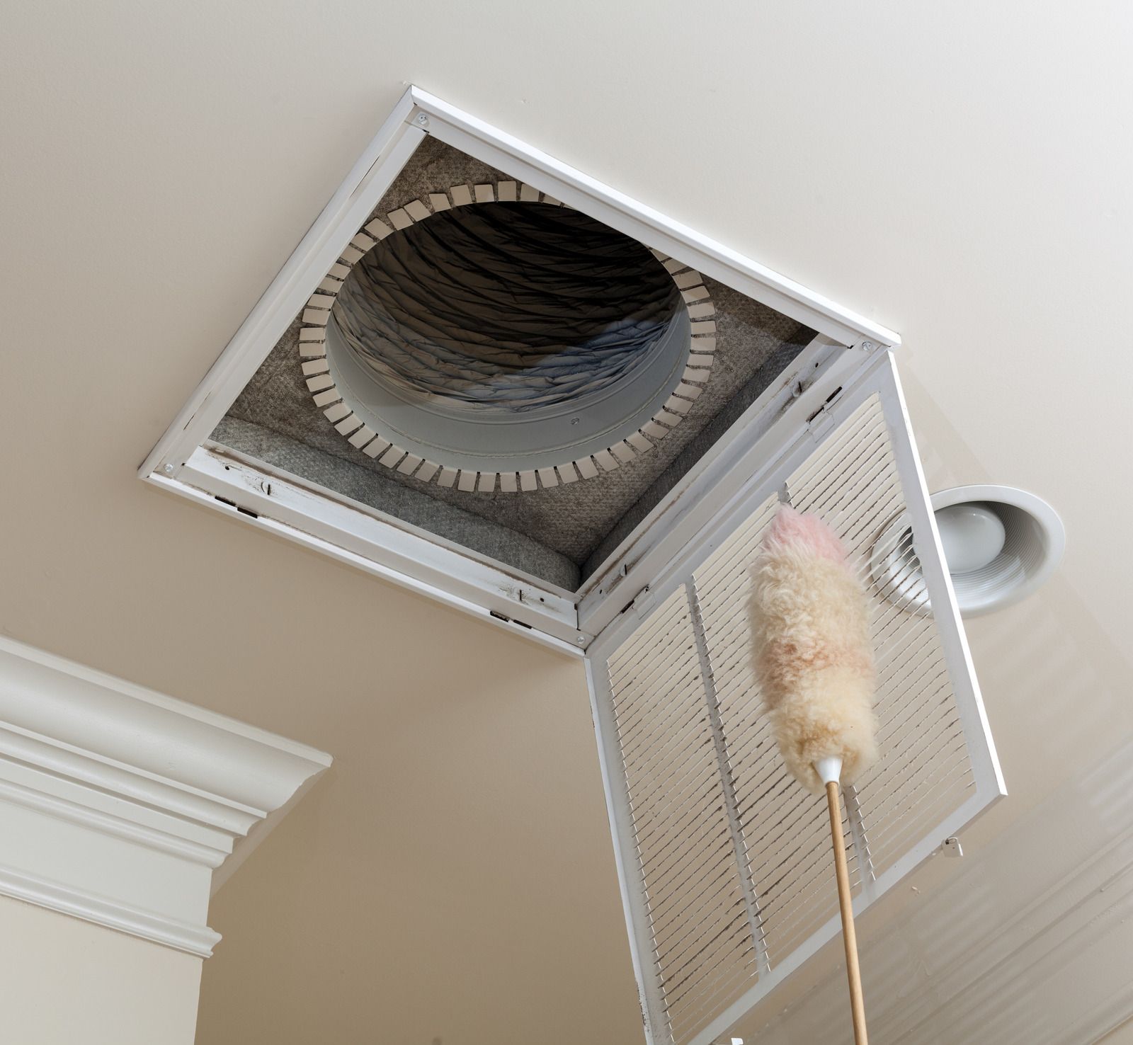 A person is cleaning an air vent with a duster.