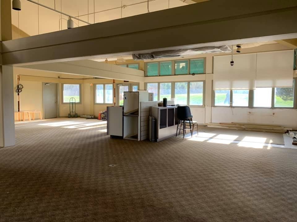 Interior view of a room under renovation with carpet, windows, and construction materials in the middle.