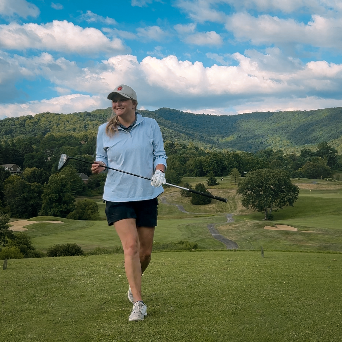 Woman on a golf course, smiling, holding club,golf course and mountain backdrop.