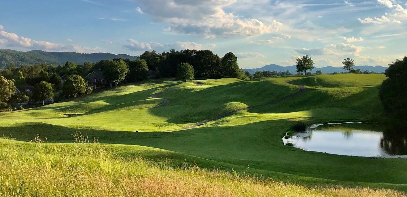 A green golf course with a small pond on a sunny day.