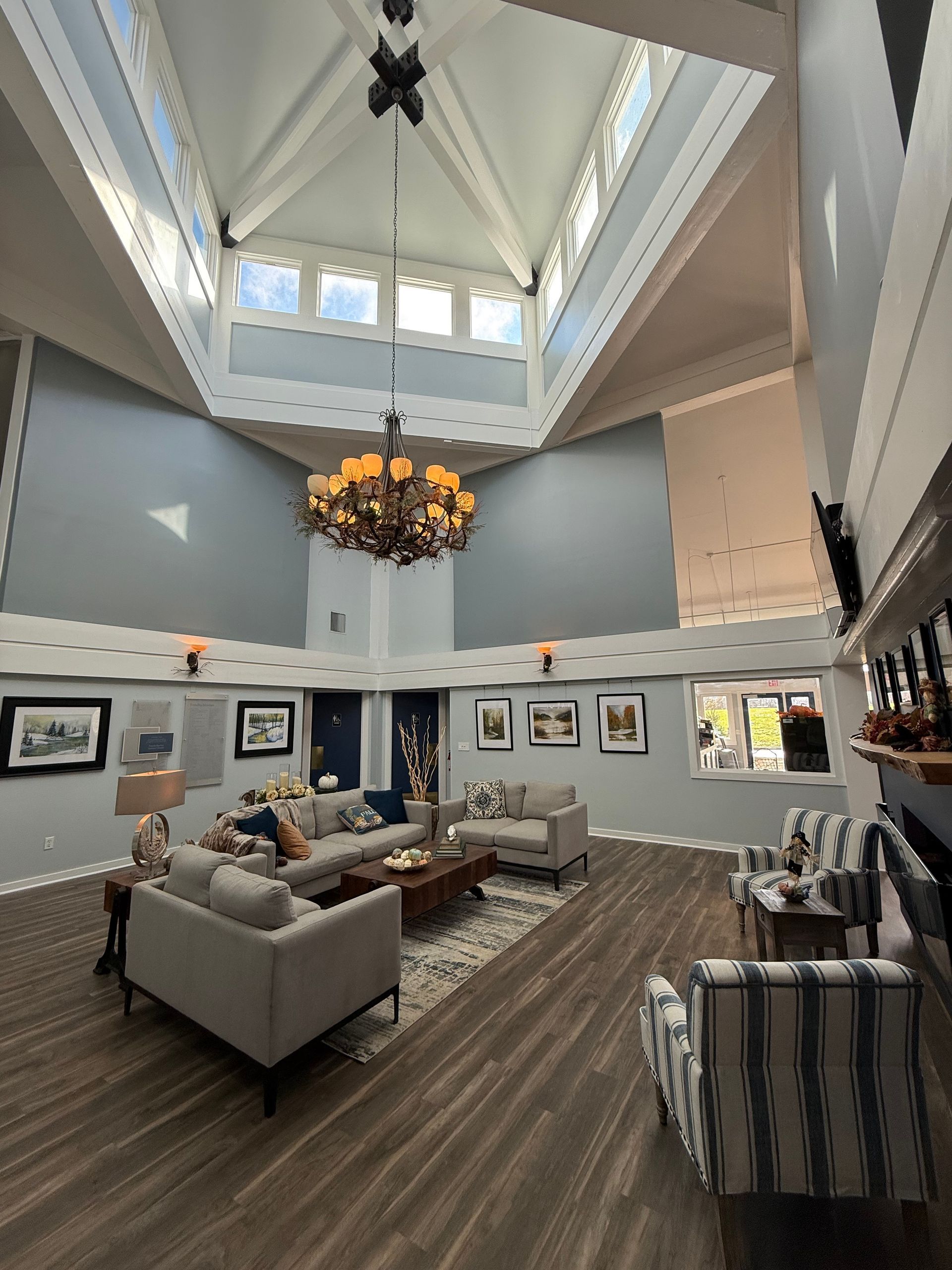 Spacious room with high ceilings, skylights, and a chandelier. Furnished with couches, armchairs, and art.