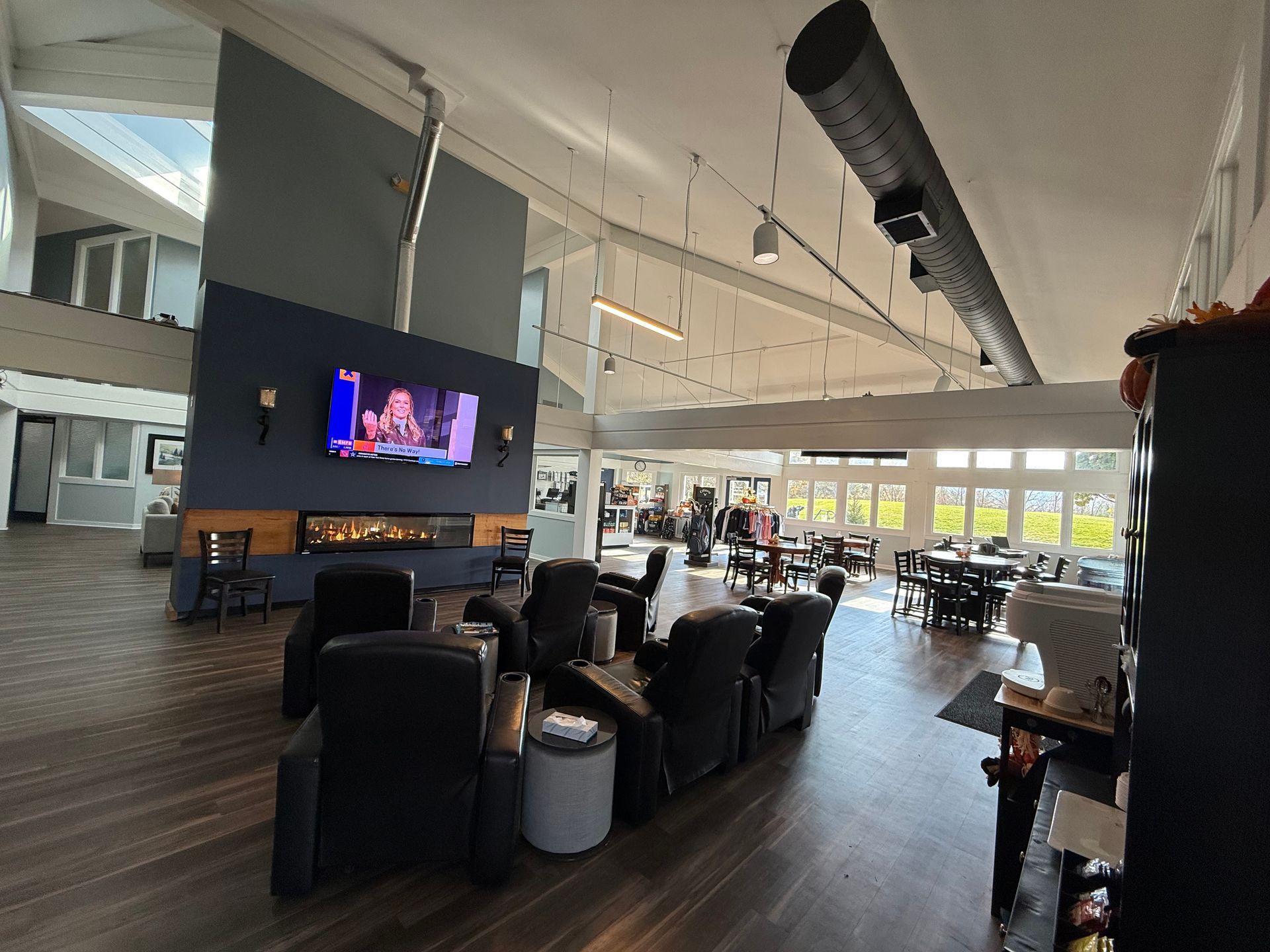 Interior of a modern lounge with fireplace, TV, seating, and tables. Bright with large windows, dark blue accent wall.