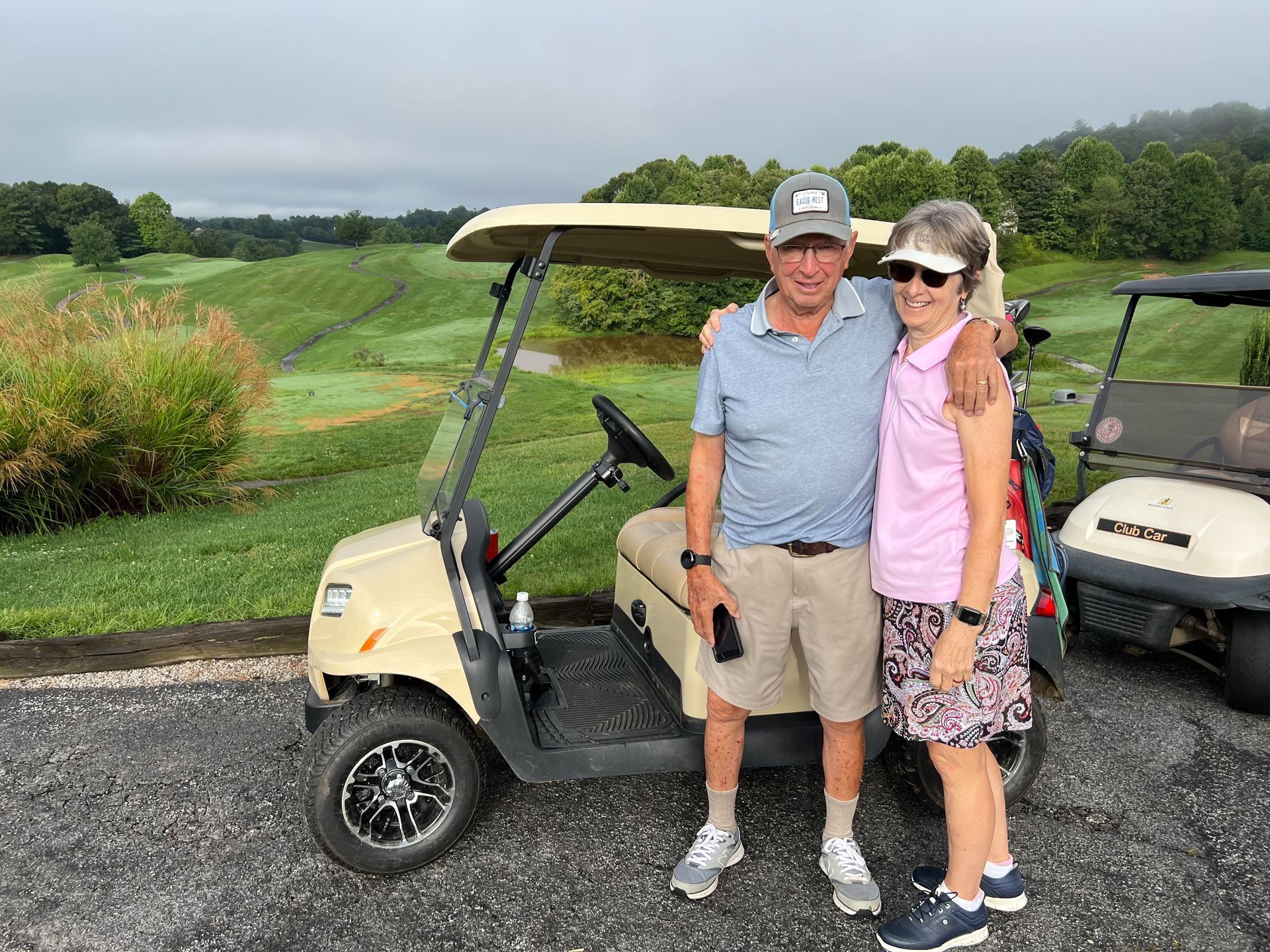 Man and woman with golf cart on a golf course, man has arm around the woman.