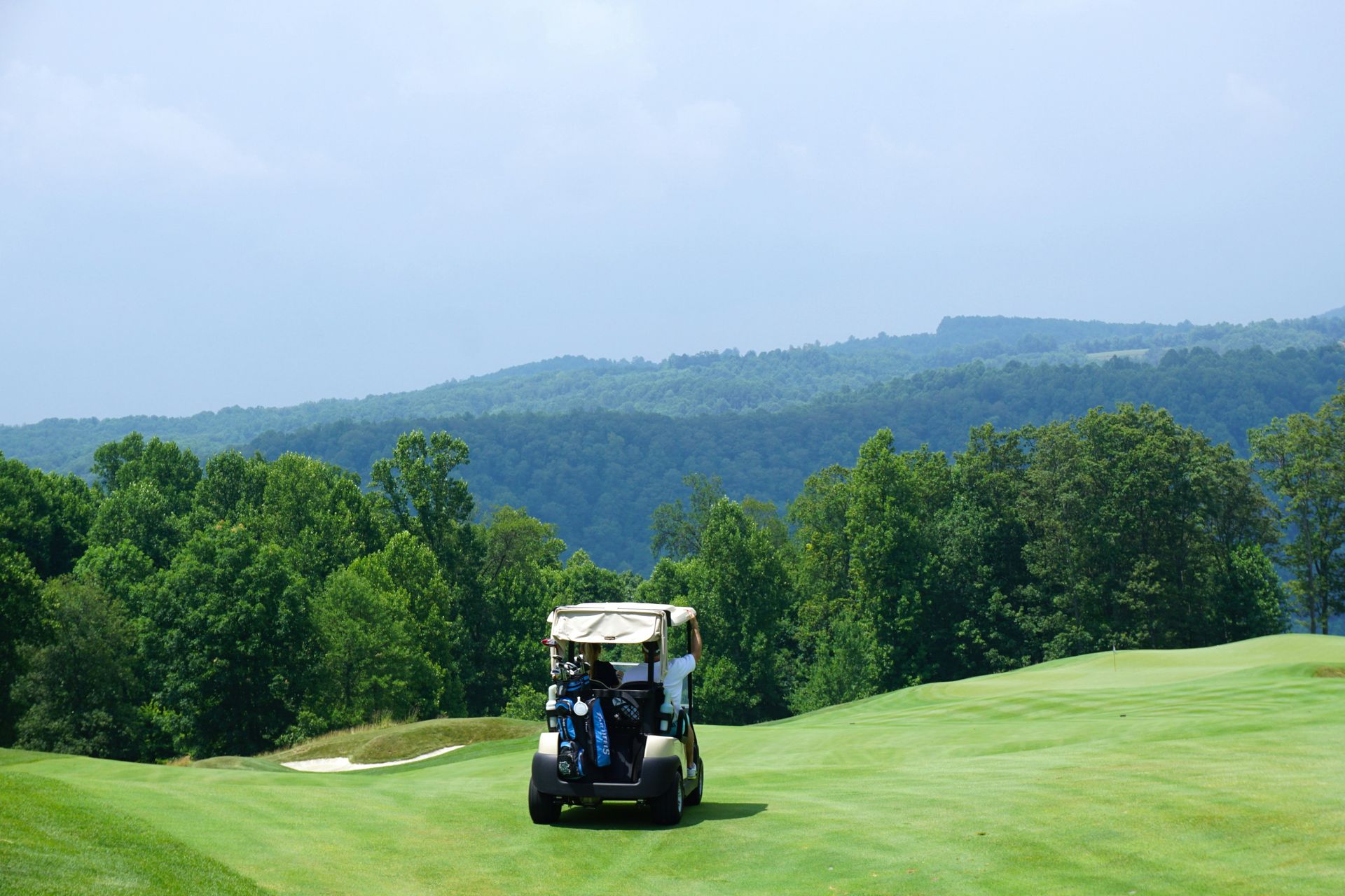 A golf cart is driving down a golf course with mountains in the background.