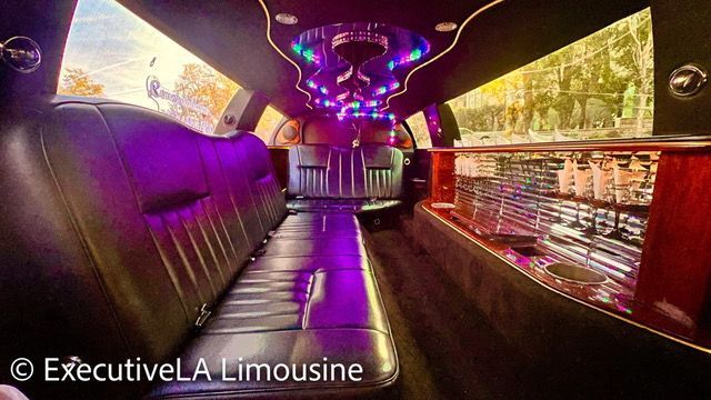 Luxury limousine interior with purple LED lights, black leather seats, and mirrored ceiling