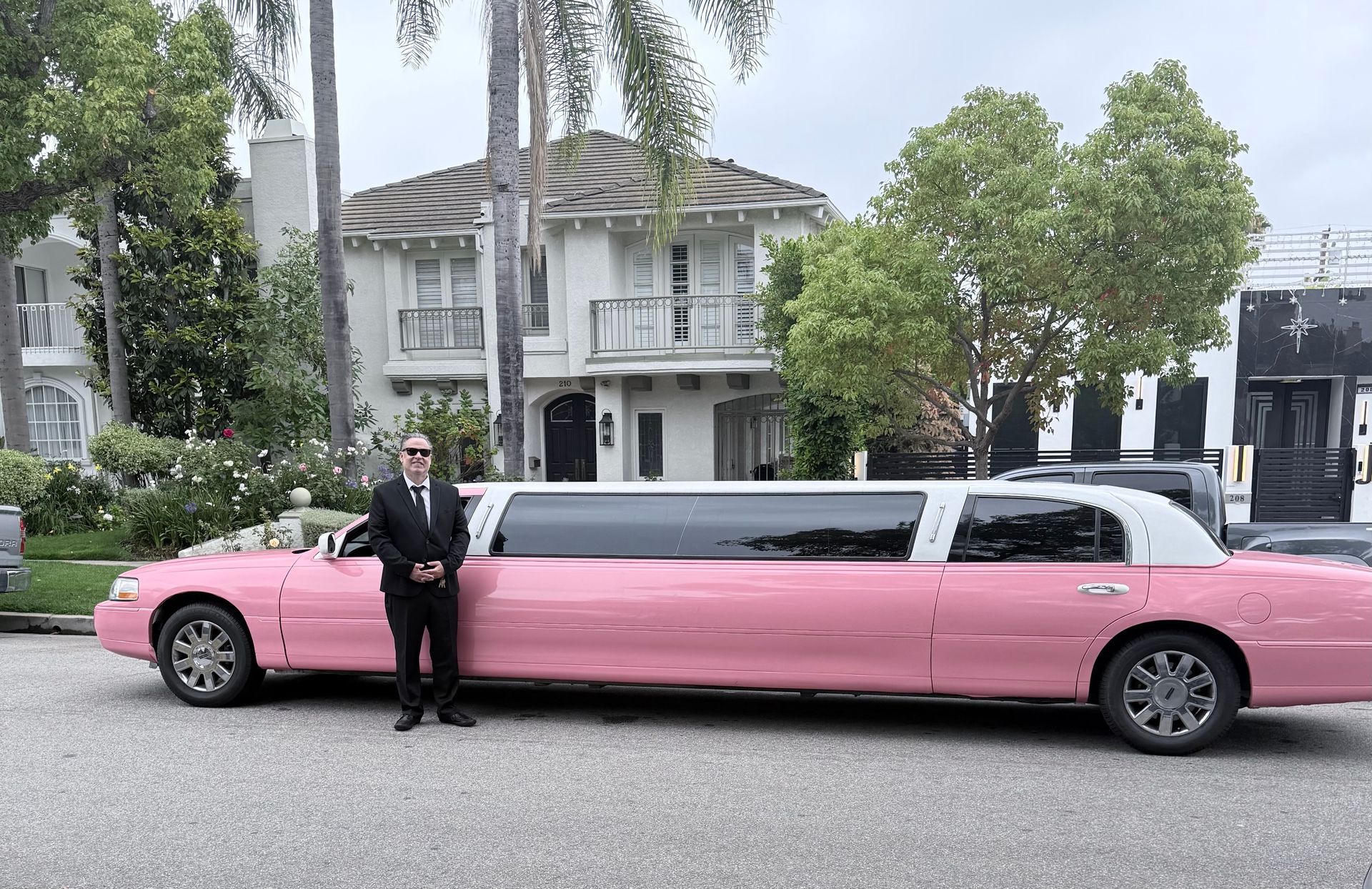 Pink stretch limousine parked on a residential street beside a person in a black suit
