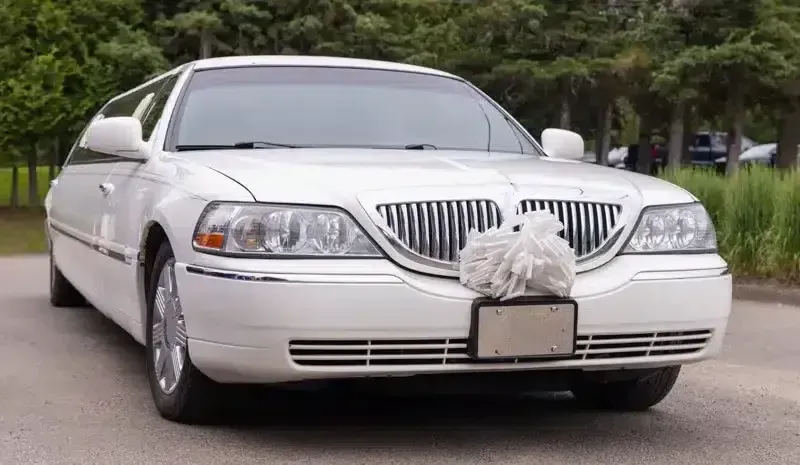 White limousine decorated with a large front bow parked on a tree-lined street