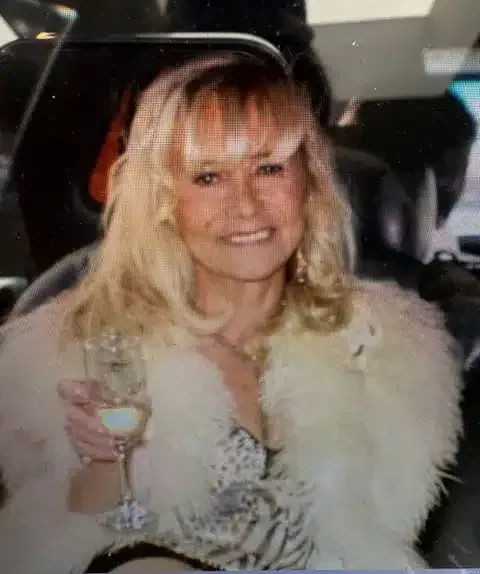 Woman smiling and holding a wine glass in a car, wearing a white fur coat.