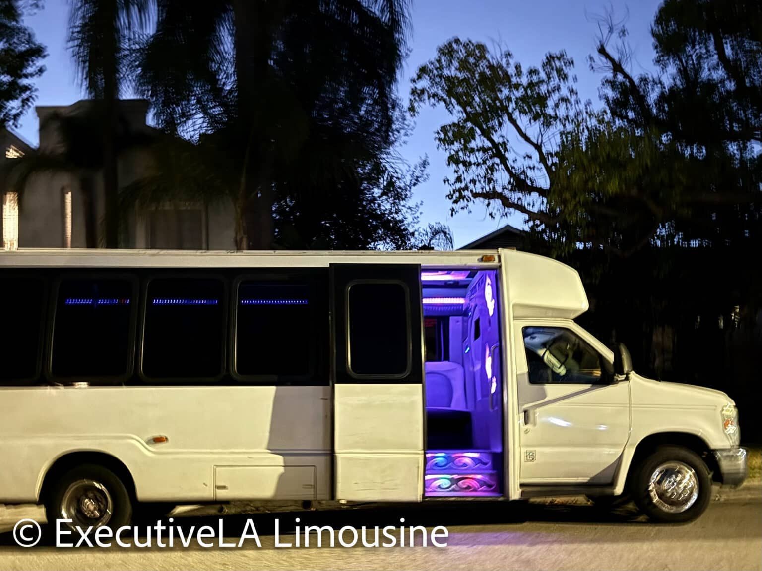 White limousine with purple-lit interior parked outdoors at dusk