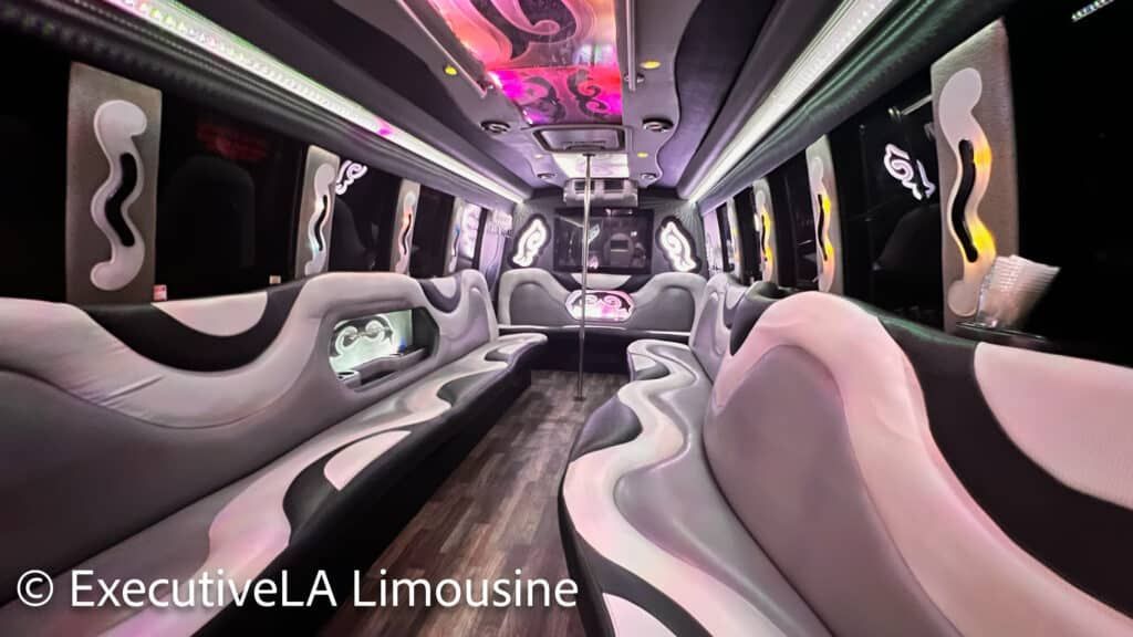 Luxury limousine interior with pink and black seats, mirrored ceiling, and neon accent lighting