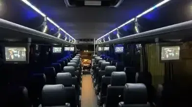 Empty bus interior with blue seats and overhead lights, viewed from the rear aisle