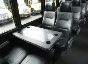 Interior of a shuttle bus with black seats and a fold-down table by the windows