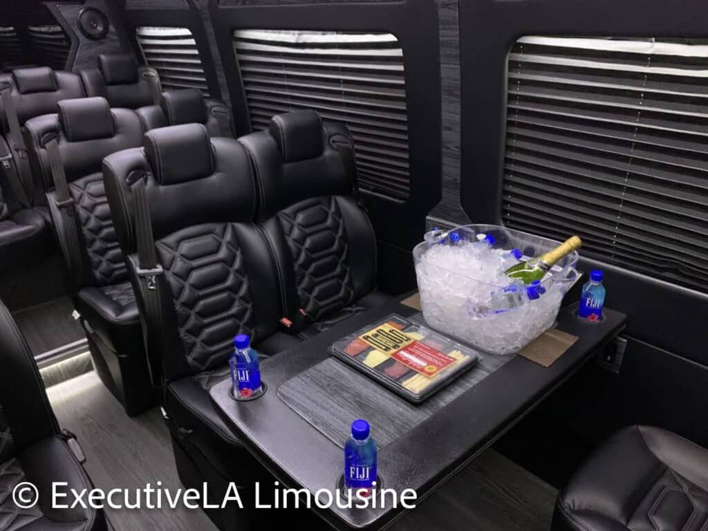 Luxury van interior with black leather seats, tray table, bottled drinks, and ice bucket