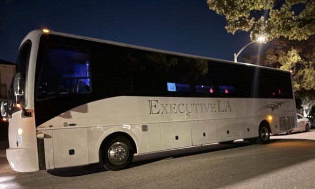 White ExecutiveLA coach bus parked on a street at night under streetlights.