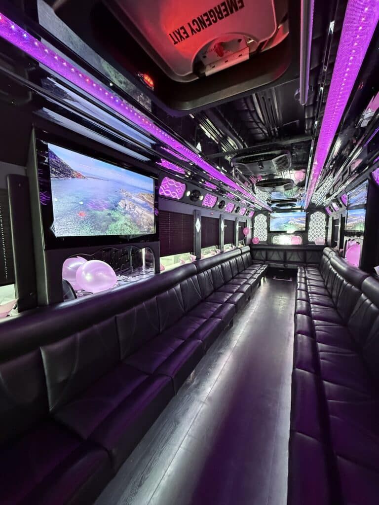 Purple-lit luxury party bus interior with black leather seats and wall-mounted screens