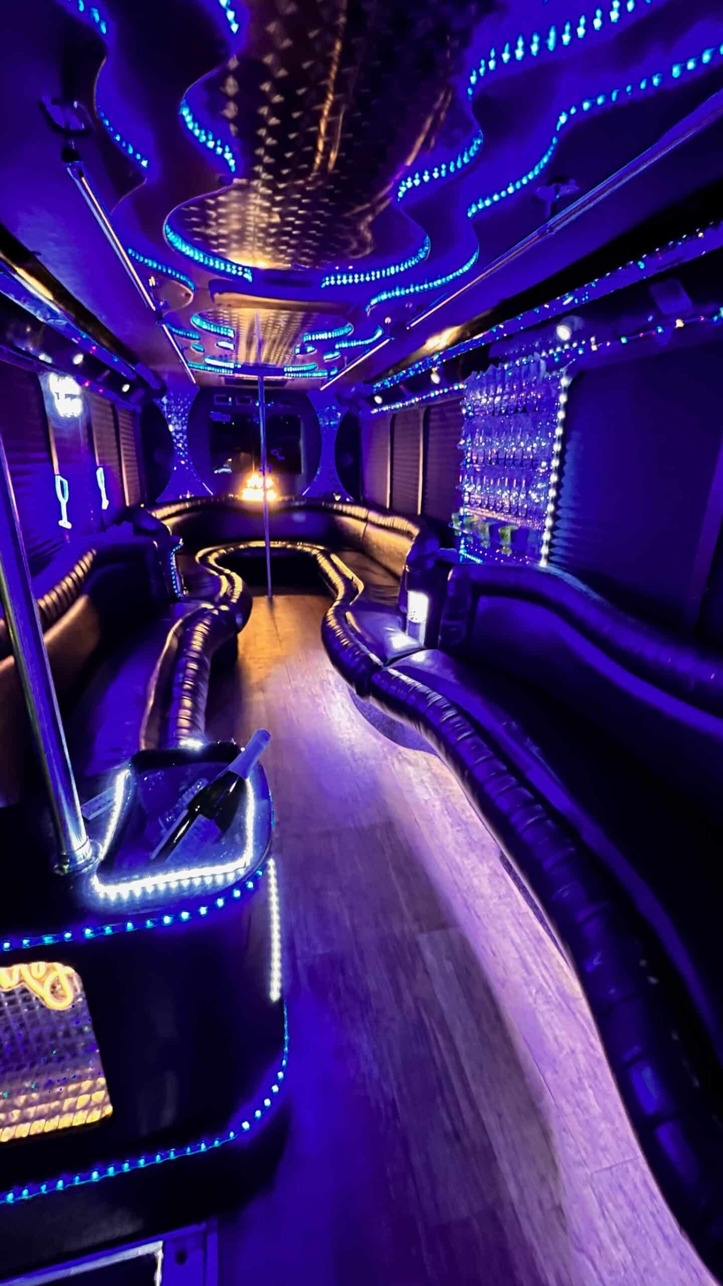 Purple-lit luxury bus interior with leather seats, neon ceiling lights, and a central aisle