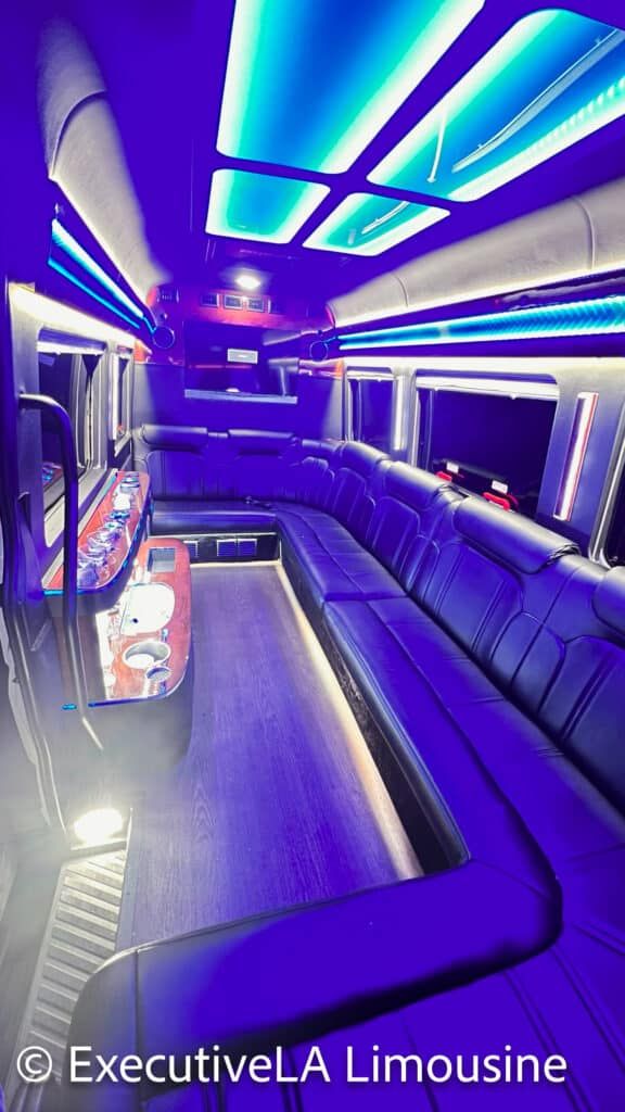Luxury limousine interior with blue and purple LED lighting, black leather seats, and a central aisle.