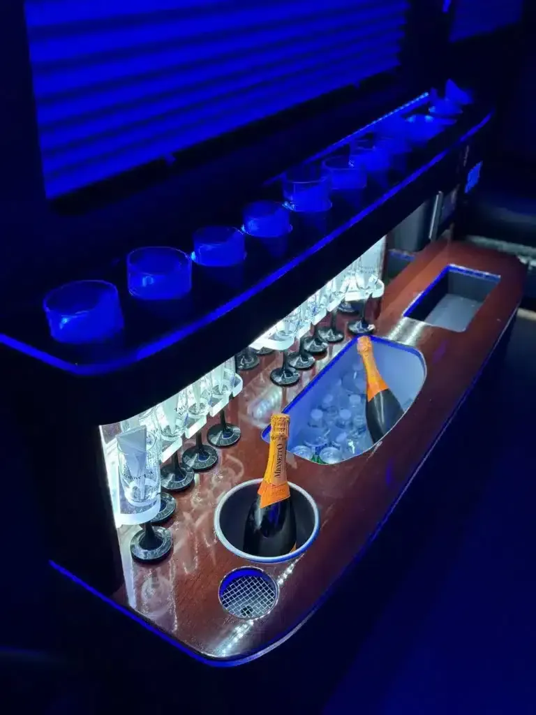 Blue-lit bar shelf with glassware, bottles, and a copper countertop, viewed at an angle