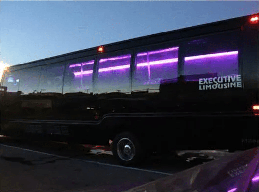 Black executive limousine bus with purple-lit windows parked at dusk