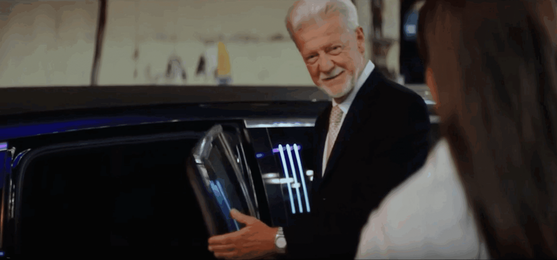 Man in a suit smiling beside an open car door at night