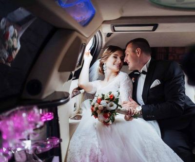 Bride and groom smiling in a decorated limousine, holding a bouquet and gazing at each other